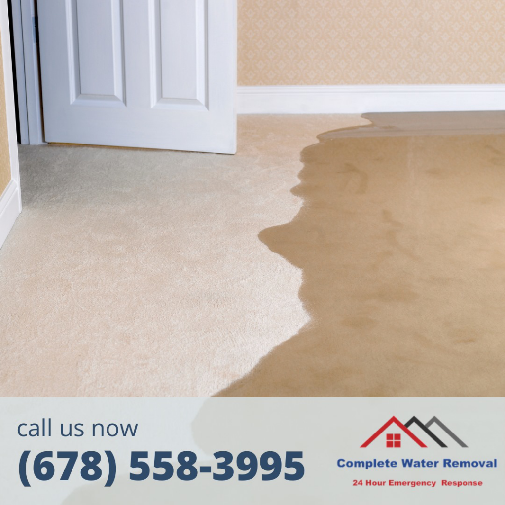 Water spreading from under a door onto a carpeted floor, indicating water damage for Complete Water Removal and Restoration in Cumming, GA.