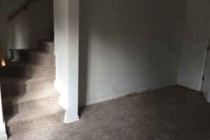 A visible water stain along the baseboard and on the carpeted floor, showing water damage requiring remediation by Local Clean Up Specialists in Green Bay, WI.