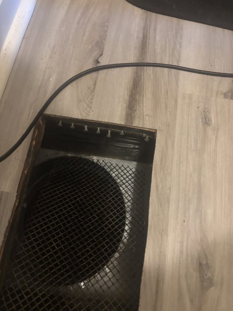 Close-up of a floor vent showing clear water stains and discoloration on the surrounding laminate flooring, indicating water damage, addressed by COIT Cleaning and Restoration in Indianapolis, IN.