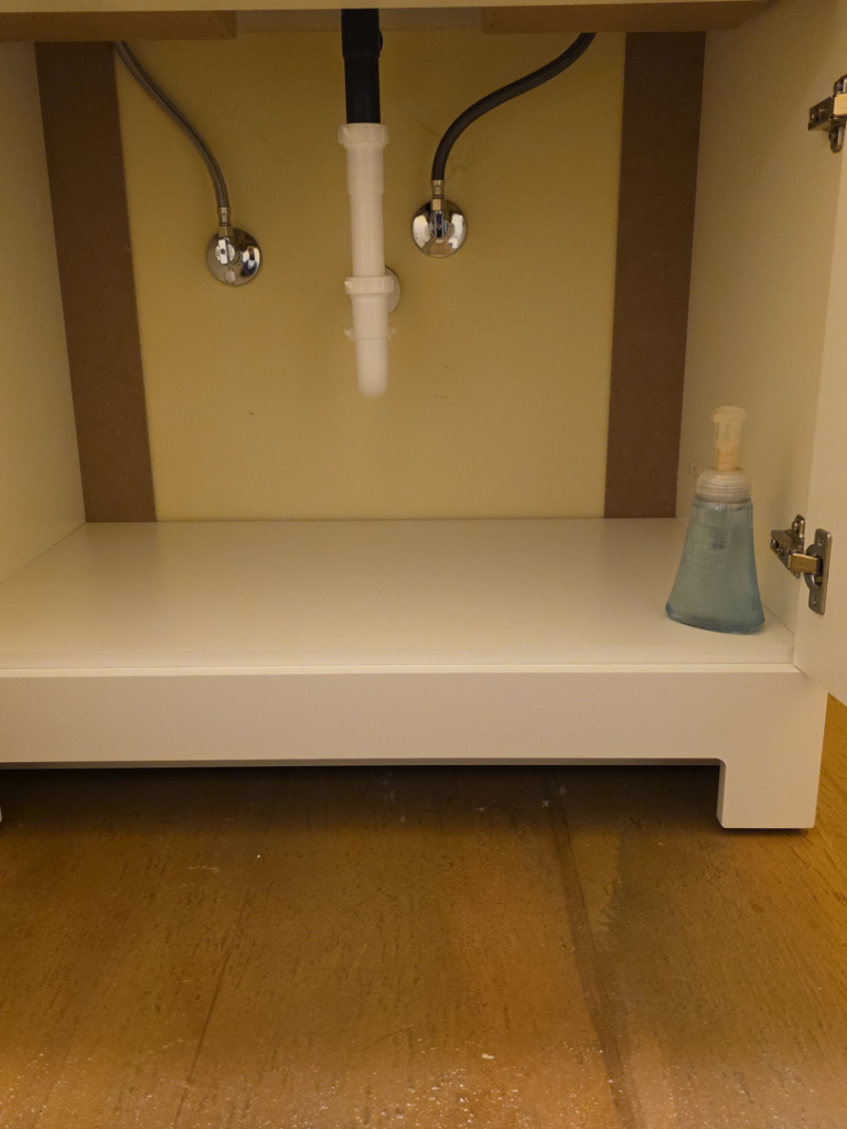 Water stains visible on the floor inside a sink cabinet, indicating a leak, repaired by JB'S Home Repair in Manhattan, KS.