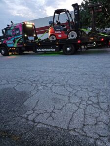 A Watkins Towing flatbed truck transporting a forklift on its bed in Augusta, GA.
