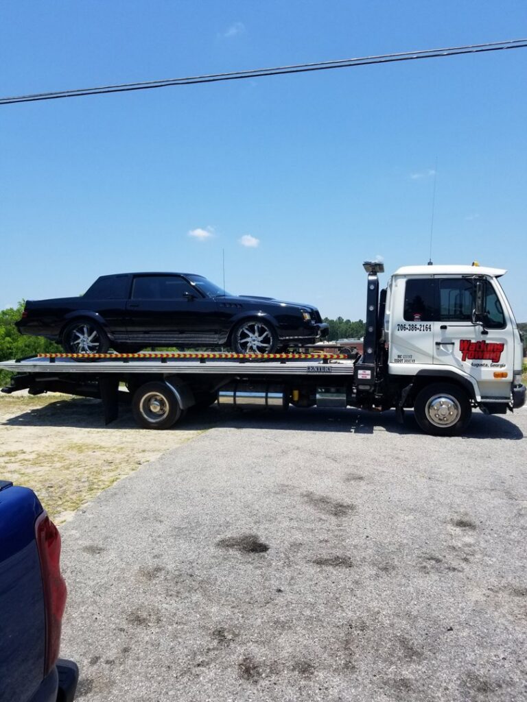 A Watkins Towing flatbed truck transporting a black car on a sunny day in Augusta, GA.