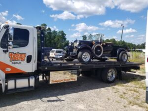 A Watkins Towing flatbed truck transporting a black classic car in Augusta, GA.