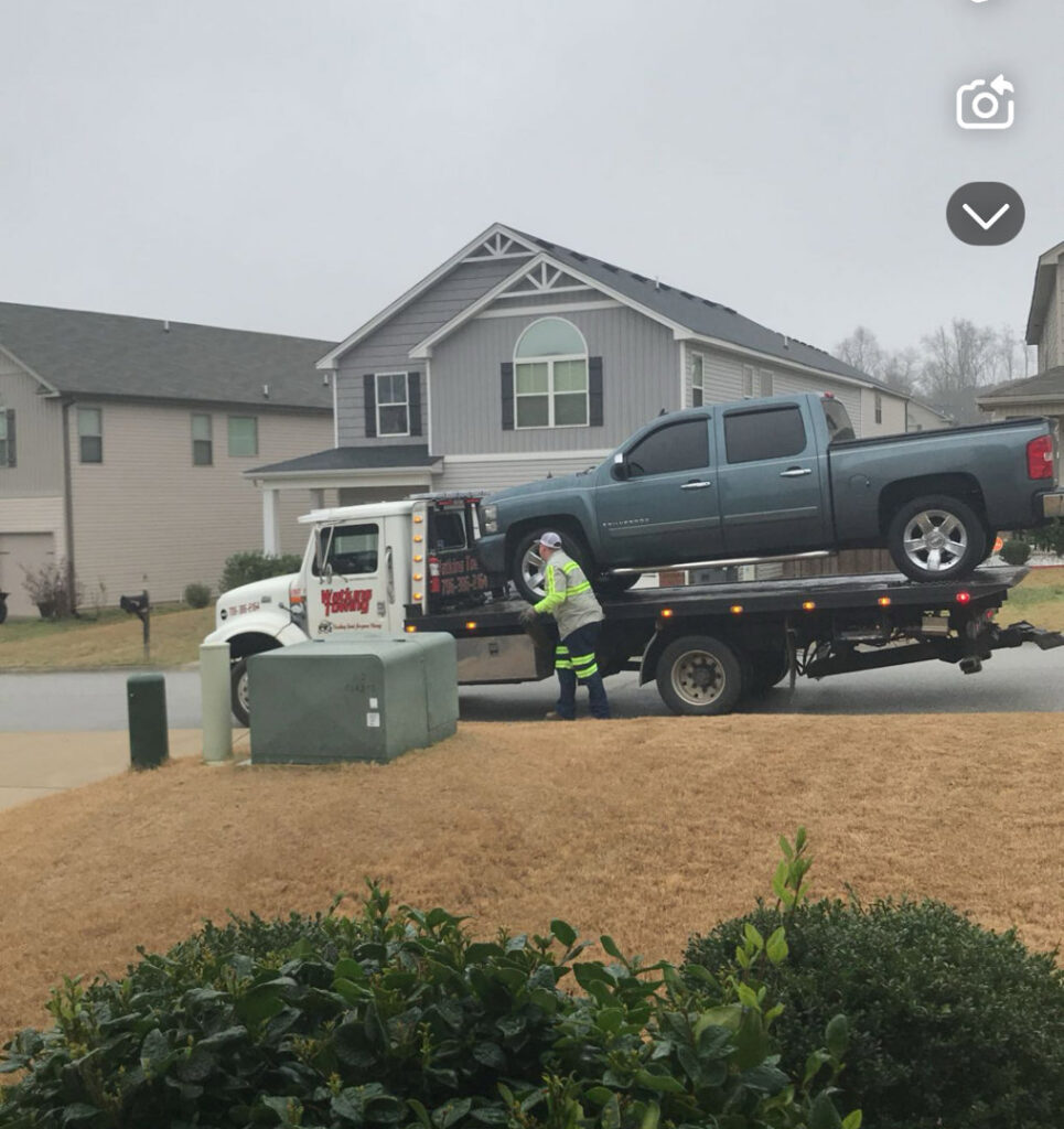 A Watkins Towing truck with a worker loading a blue pickup truck onto its flatbed in Augusta, GA.