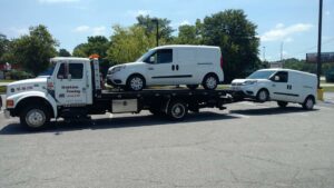 A Watkins Towing truck transporting two white vans, one on the flatbed and one towed behind, in Augusta, GA.