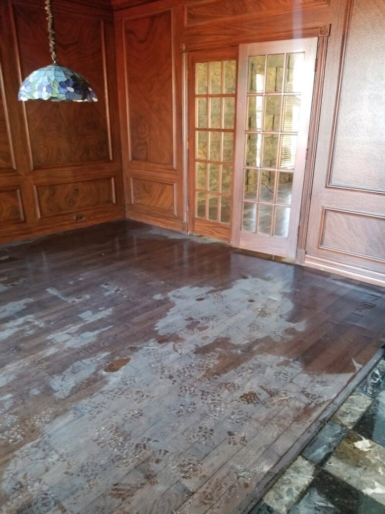 Room with dark hardwood floors showing wet footprints and water marks, indicating water damage, by Dakota Fire and Water Restoration in Bismarck, ND