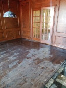 A room with wet wooden floors and visible footprints in the standing water, clearly showing water damage requiring restoration by Dakota Fire and Water Restoration in Bismarck, ND.