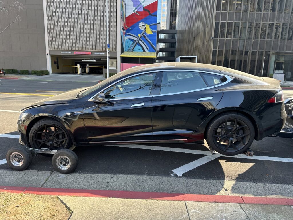 A black Tesla sedan being towed by a wheel lift tow truck with dollies by R towing Services in Sacramento, CA.