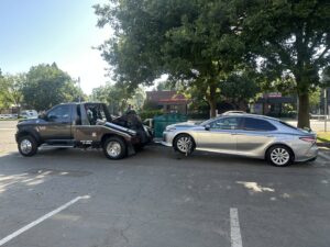 A silver sedan being towed by a wheel lift tow truck by R towing Services in Sacramento, CA.