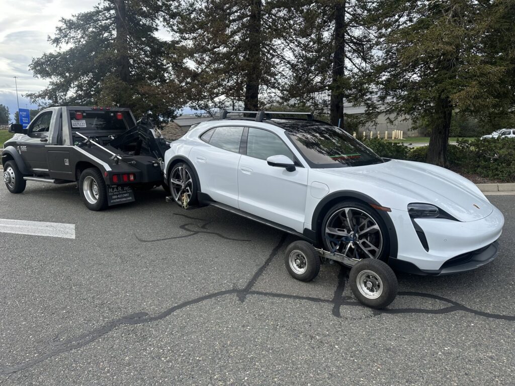 A white Porsche car being towed by a wheel lift tow truck with dollies by R towing Services in Sacramento, CA.