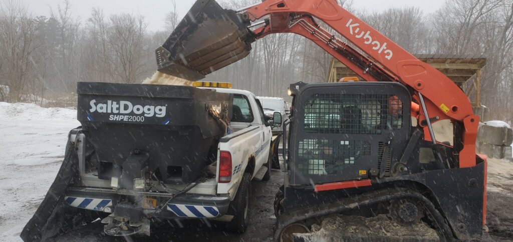 A large yellow wheel loader actively moving snow in a commercial parking lot by TPM Snow Removal in Schenectady, NY.