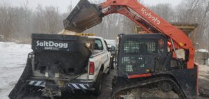 A large yellow wheel loader actively moving snow in a commercial parking lot by TPM Snow Removal in Schenectady, NY.