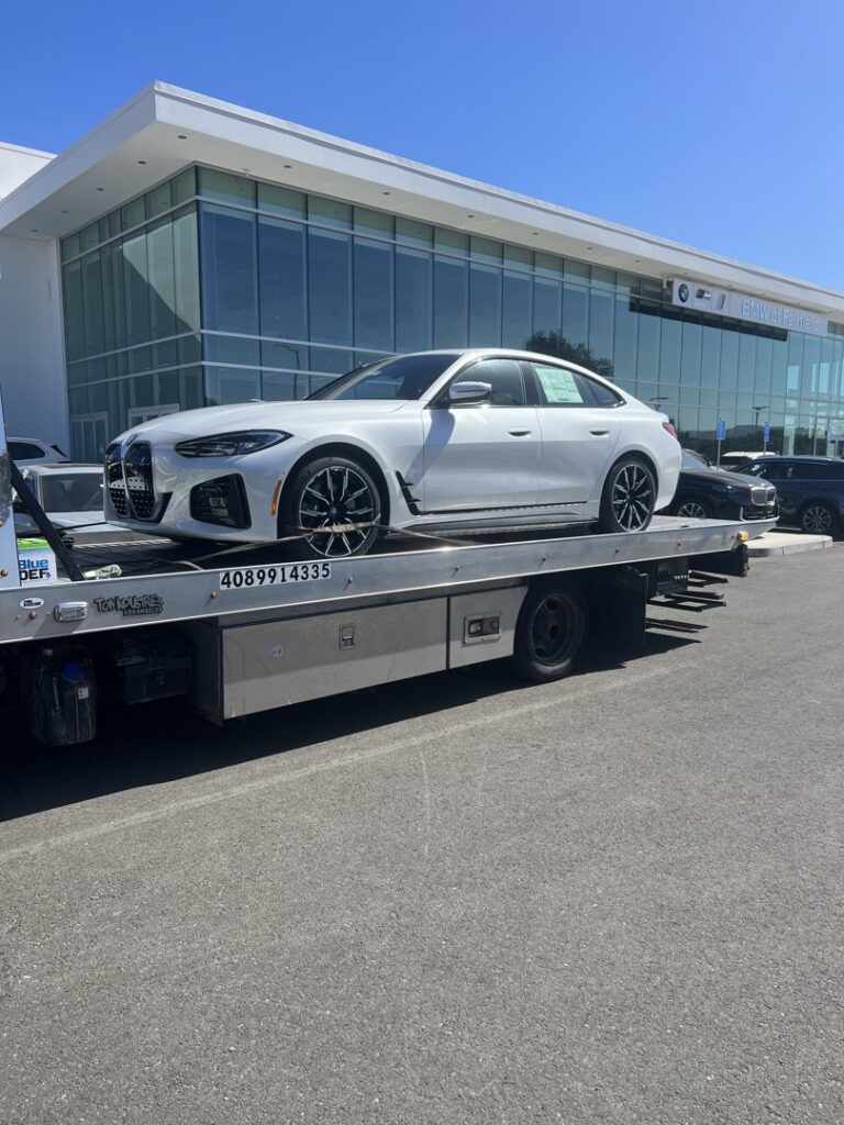 A white BMW sedan being transported on a flatbed tow truck by 101 auto towing inc in San Jose, CA.