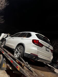 A white BMW SUV being towed on a flatbed tow truck at night by Black Rhino Towing in Denver, CO.