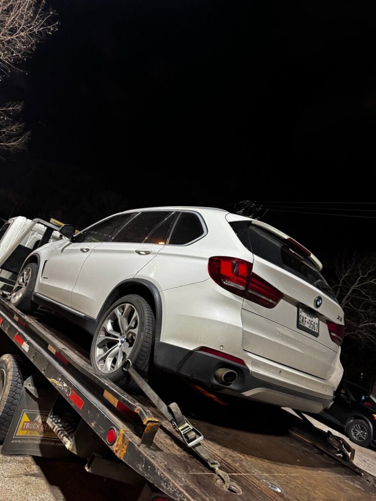 A white BMW SUV being towed on a flatbed tow truck at night by Black Rhino Towing in Denver, CO.