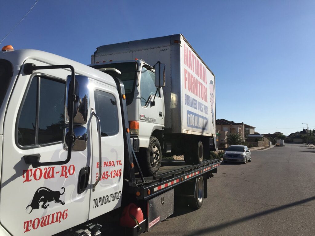 A white box truck being transported on a flatbed tow truck by Tow-Ro Towing in El Paso, TX.