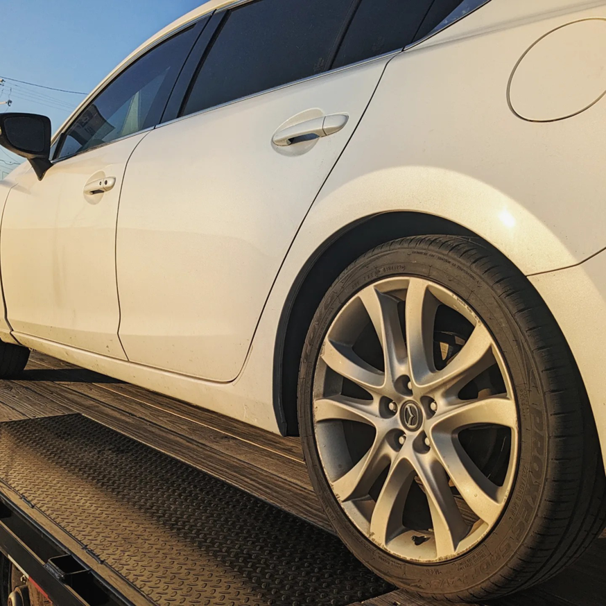 A white car loaded onto a flatbed tow truck by Mountain Goat Rescue & Recovery LLC + Towing in Nampa, ID.