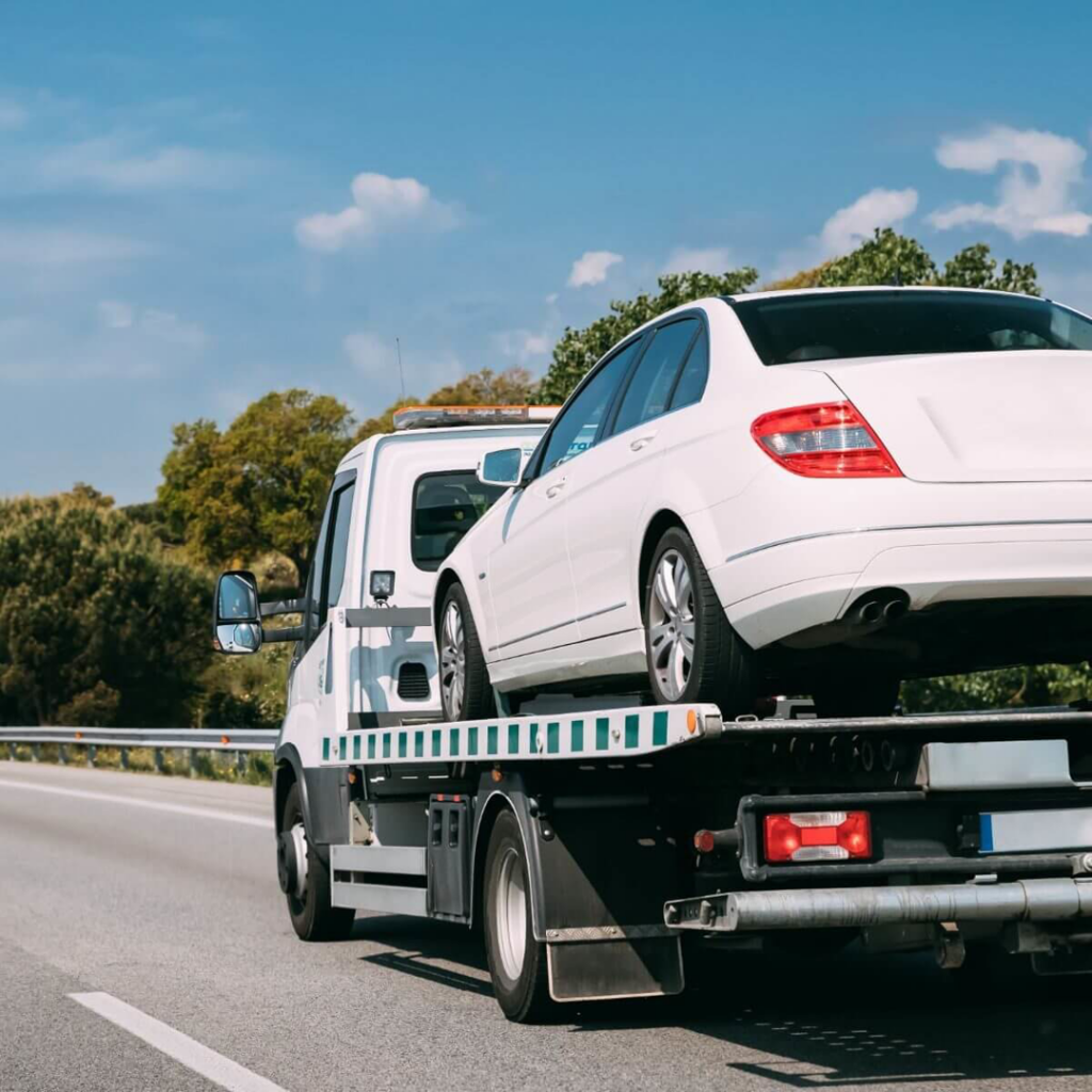 A white sedan being transported on a flatbed tow truck by Safelane Towing Services Co. in Layton, UT.