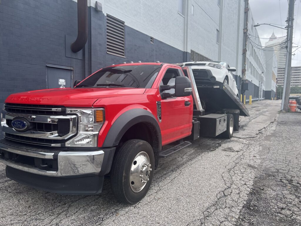 A white car being transported on a flatbed tow truck in an urban alleyway by Quiñones Towing in Cleveland, OH.