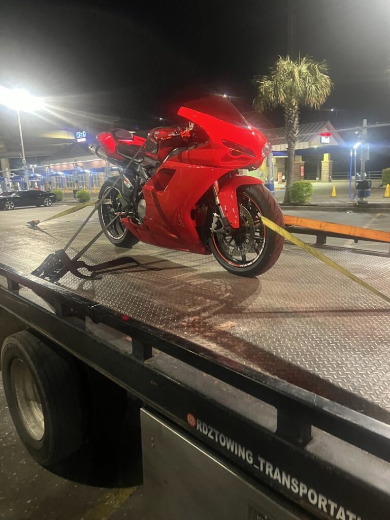 A white car with a missing wheel being loaded onto a flatbed tow truck at night for RDZ Towing Service 24/7 in Dallas, TX.