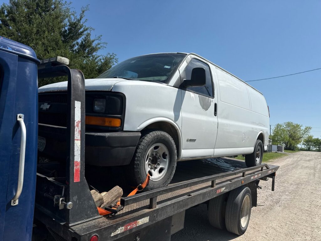 A white cargo van being towed on a flatbed tow truck by Black Rhino Towing in Denver, CO.