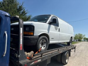 A white cargo van being towed on a flatbed tow truck by Black Rhino Towing in Denver, CO.