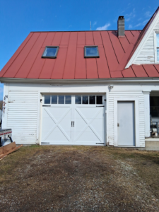 A newly installed white carriage-style garage door with decorative hardware by Ski Door, Inc. in Center Rutland, VT.
