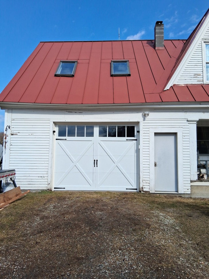 A newly installed white carriage-style garage door with decorative hardware by Ski Door, Inc. in Center Rutland, VT.