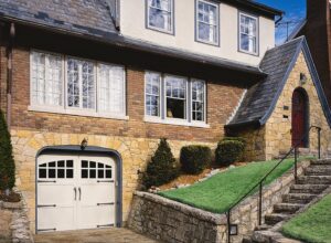 A charming white carriage-style garage door with decorative hardware in a stone archway by The Door Man - Garage Doors & Openers in Reno, NV