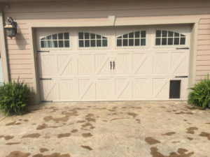 A white carriage-style garage door with windows and a pet door by Advantage Door Company in Troy, MO.