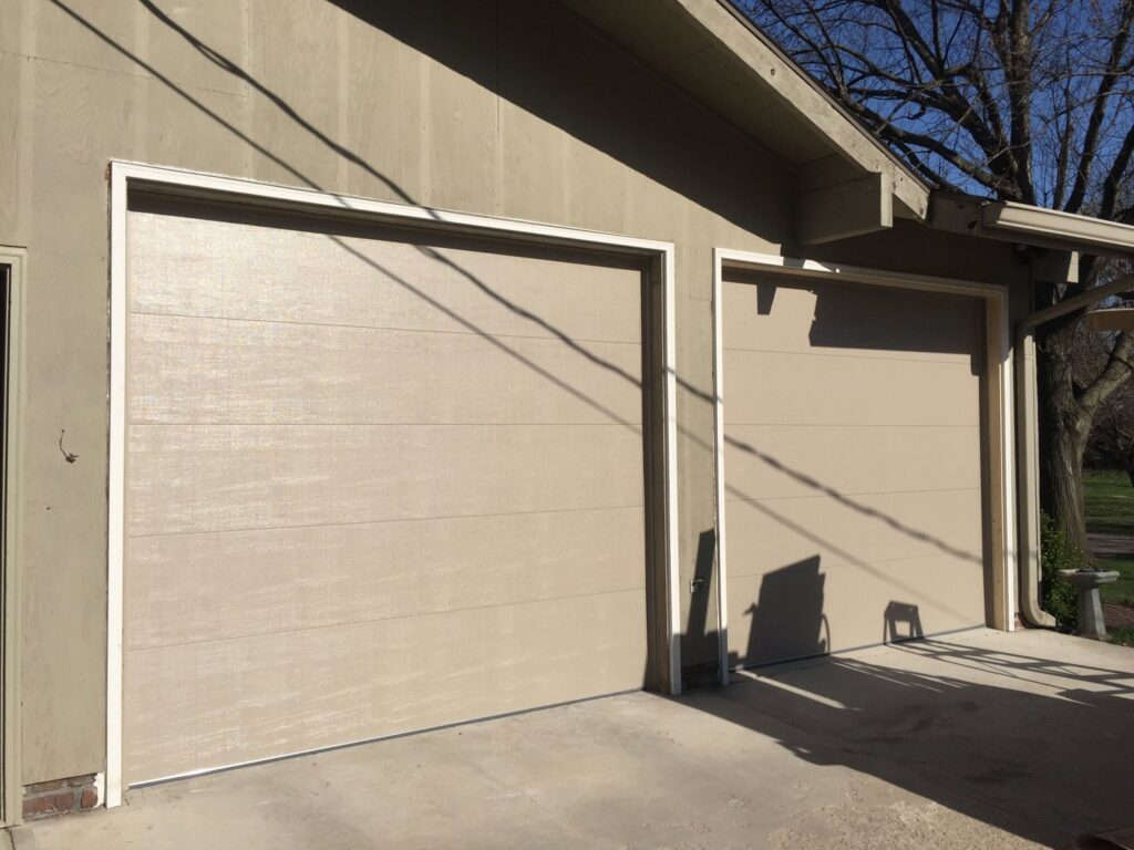 A yellow house featuring two white carriage-style garage doors with decorative hardware, installed by JLM Garage Doors Omaha in Papillion, NE.
