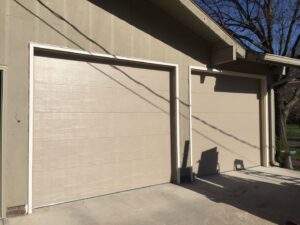 A yellow house featuring two white carriage-style garage doors with decorative hardware, installed by JLM Garage Doors Omaha in Papillion, NE.