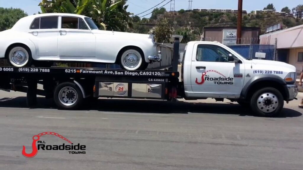 A white classic car being transported on a flatbed tow truck by All Roadside Towing San Diego, CA.