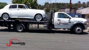 A white classic car being transported on a flatbed tow truck by All Roadside Towing San Diego, CA.