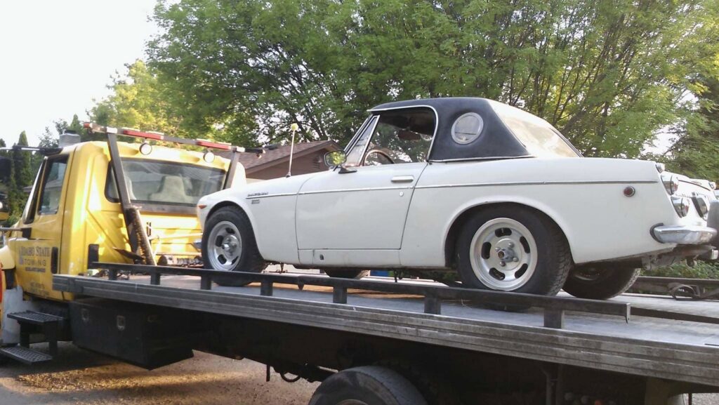A white classic convertible car being transported on a flatbed tow truck by Idaho State Towing and Recovery in Caldwell, ID.