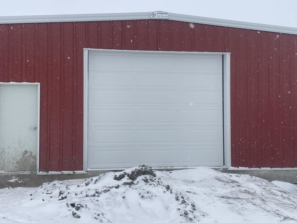 A white commercial garage door installed on a red metal building by PS Garage Doors of Williston, ND.