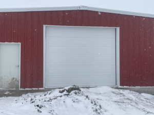 A white commercial garage door installed on a red metal building by PS Garage Doors of Williston, ND.