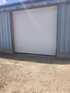 A white commercial roll-up garage door on a metal building, installed by Doors & more,inc in Quincy, IL