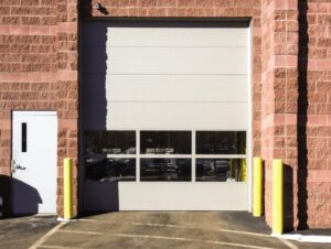 A white commercial sectional garage door with windows installed on a brick building by Wayne Dalton Sales & Service of Quad Cities in Davenport, IA.