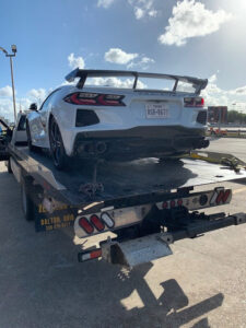 A white Corvette sports car being transported on a flatbed tow truck by Jay Towing Services in Houston, TX.