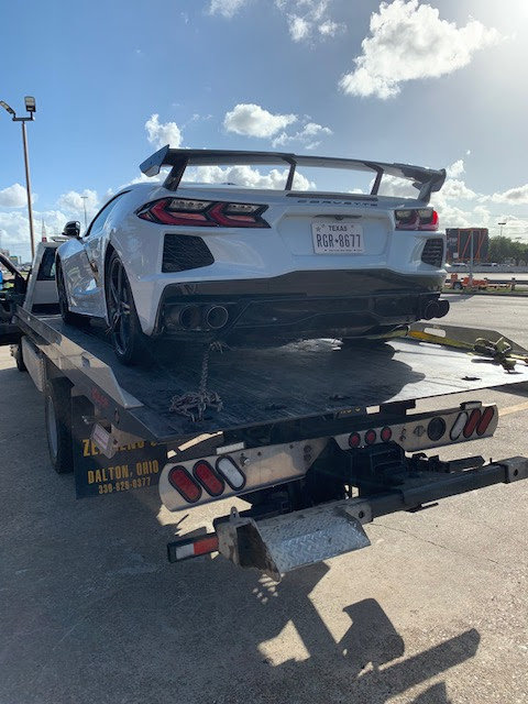 A white Corvette sports car being transported on a flatbed tow truck by Jay Towing Services in Houston, TX.