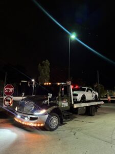 A white Dodge Challenger loaded onto a flatbed tow truck from Bullcity Towing & Services LLC at night in Durham, NC.