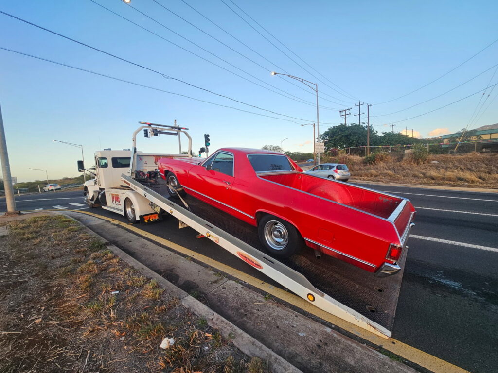A white Tip Tows flatbed tow truck loading a red vintage car for towing services in Honolulu, HI.