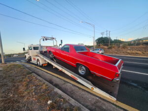 A white Tip Tows flatbed tow truck loading a red vintage car for towing services in Honolulu, HI.