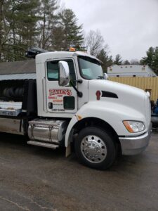 A white flatbed tow truck from Bailey's Towing and Auto Body, LLC parked at its facility in Merrimack, NH.