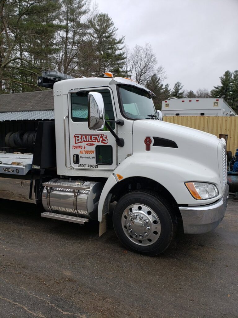 A white flatbed tow truck from Bailey's Towing and Auto Body, LLC parked at its facility in Merrimack, NH.