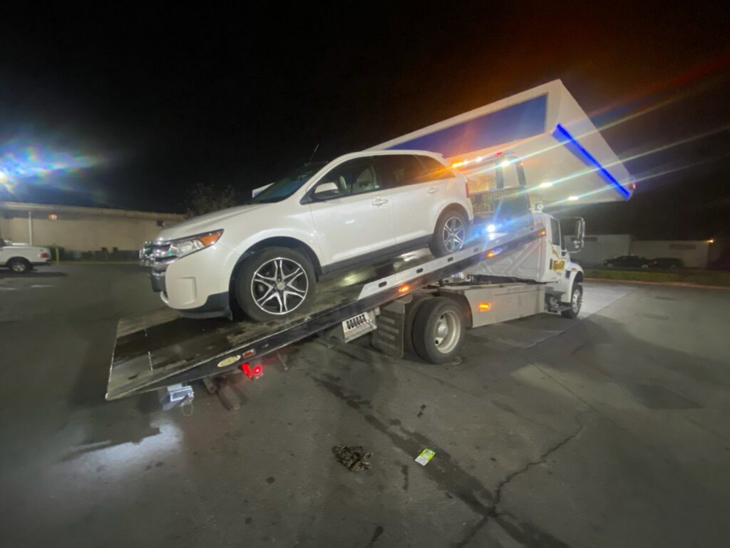 Aguilar Towing's white flatbed tow truck transporting a white SUV at night in San Jose, CA