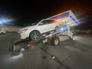 Aguilar Towing's white flatbed tow truck transporting a white SUV at night in San Jose, CA
