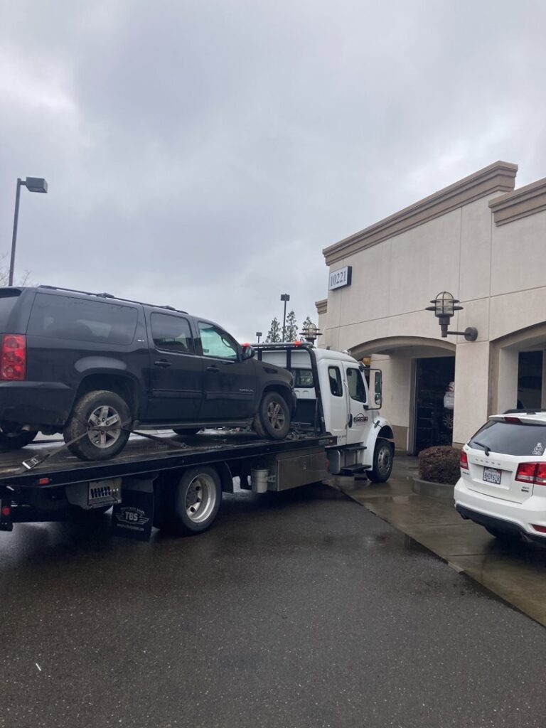 A white flatbed tow truck from Anthony's Towing & Transportation transporting a black SUV in Yuba City, CA.