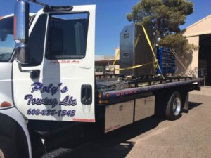 A white flatbed tow truck from Poly's Towing Glendale transporting large industrial equipment in Glendale, AZ.